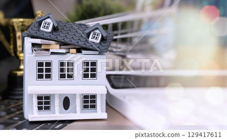 Miniature house filled with money and gold bars, placed on a keyboard with shopping cart and trophy in background, symbolizing financial success. Miniature house filled with money and gold bars, placed on a keyboard with shopping cart and trophy in background, symbolizing financial success. 129417611