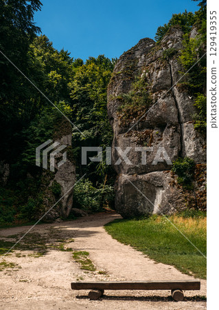 Wide hiking path leading between towering rock formations and dense green forest on a clear sunny day. Nature trail access, geotourism, protected landscapes, outdoor recreation infrastructure 129419355