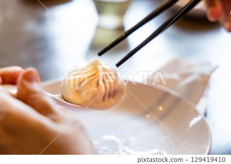 Diner picking up Shanghai popular xiaolongbao or little dragon dumpling with spoon and chopsticks 129419410