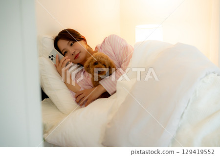Young woman operating a smartphone in bed Young woman operating a smartphone in bed 129419552