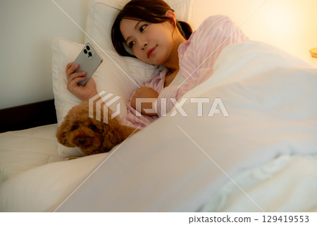 年輕女子在床上操作智慧型手機 年輕女子在床上操作智慧型手機 129419553