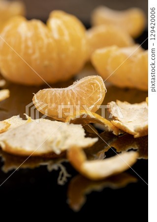 the reflection of an orange citrus tangerine in a black mirror surface, a peeled and juicy tangerine on a black mirror 129420006