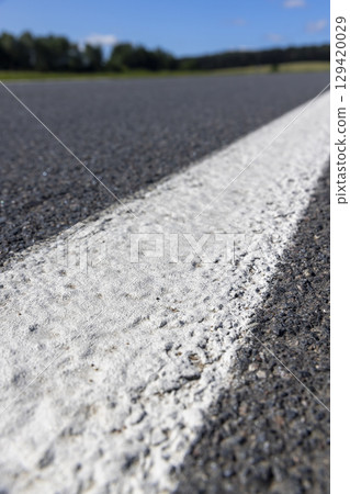 road during the day in sunny weather, paved road for vehicles with white road markings, close up 129420029
