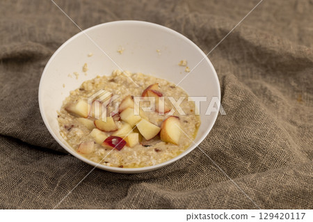 peach in oatmeal, quickly cooked oatmeal porridge with dried fruits and berries and pieces of fresh peach, closeup 129420117