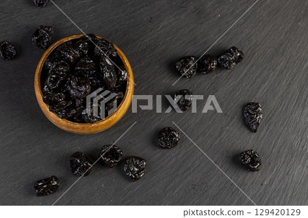 wooden bowl filled with dried prunes, dark dried plum fruits poured into a bowl on slate wooden bowl filled with dried prunes, dark dried plum fruits poured into a bowl on slate 129420129