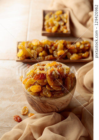 Yellow sultana raisins in a wooden bowl on a beige background. Yellow sultana raisins in a wooden bowl on a beige background. 129420962