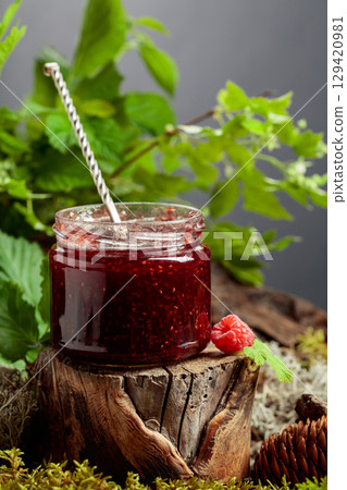 A jar of raspberry jam with fresh berries on an old tree trunk in the forest. A jar of raspberry jam with fresh berries on an old tree trunk in the forest. 129420981