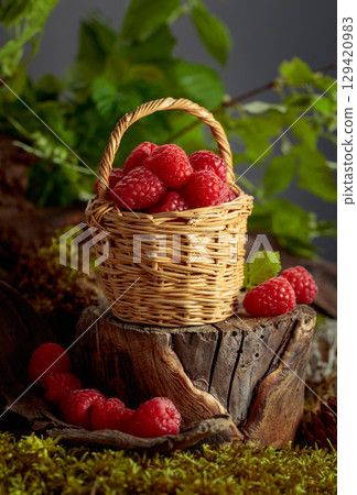 Small wicker basket filled with fresh, ripe raspberries. 129420983