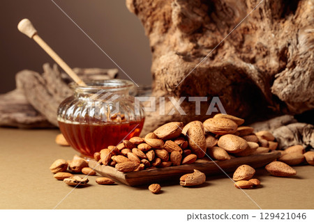 Almond nuts in a wooden dish and honey in a glass jar. Almond nuts in a wooden dish and honey in a glass jar. 129421046