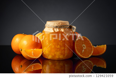 Orange jam in glass jar and fresh fruits on a black reflective background. Orange jam in glass jar and fresh fruits on a black reflective background. 129421059