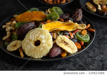 Dried tropical fruits, nuts, and raisins in black plate. Dried tropical fruits, nuts, and raisins in black plate. 129421066