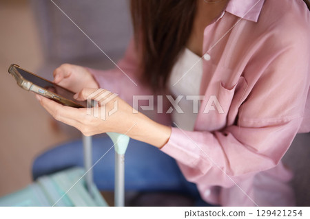 Adult Asian woman navigates smartphone for travel preparation digital communication near luggage planning next adventure 129421254