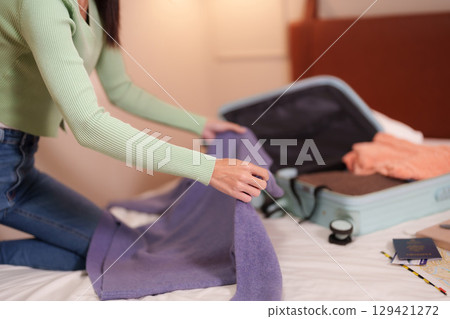 Adult woman packing suitcase travel clothes preparing for vacation in hotel room organizing luggage journey adventure getaway destination 129421272