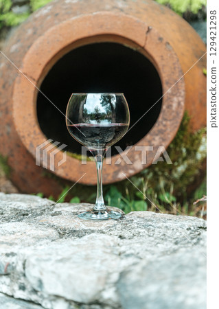 Glass of Red Wine with Traditional Georgian Qvevri in Rustic Setting 129421298