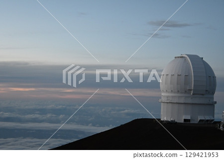 A telescope floating in a sea of clouds, tinted by the setting sun 129421953