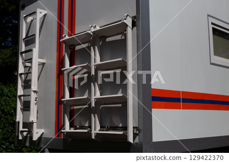 Close up of side of emergency rescue vehicle showing mounted ladder and storage racks. The bright orange and blue stripes, along with functional design, emphasize its role in emergency operations 129422370