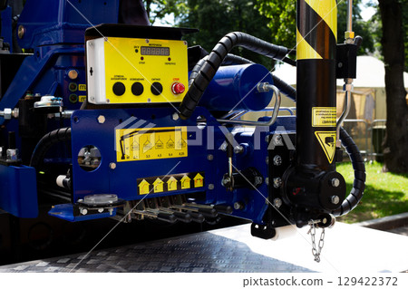 Close up shot of the control panel and hydraulic components on a construction crane. The image showcases detailed equipment with technical labels, buttons, and a safety warning on the machine 129422372