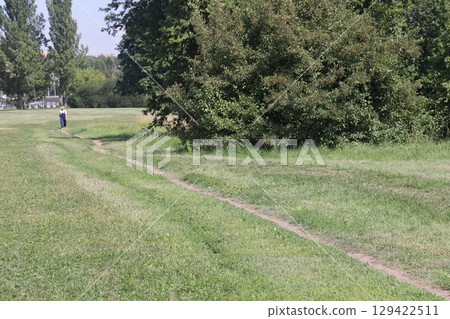 People walking on a trail in an open green field. 129422511