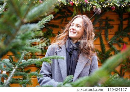 Woman smiling near Christmas tree at festive holiday market street 129424127