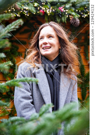 Smiling woman in winter coat near Christmas tree decorations outdoor Smiling woman in winter coat near Christmas tree decorations outdoor 129424132