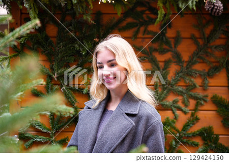 Blonde woman smiling near decorated Christmas tree at holiday market Blonde woman smiling near decorated Christmas tree at holiday market 129424150