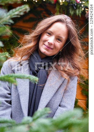 Woman in gray coat smiling near Christmas decorations outdoors 129424164