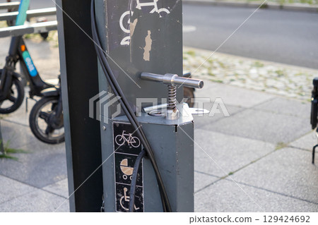 Grey public bike pump station stands outdoors, offering convenient air for bicycles, strollers, and wheelchairs in urban areas 129424692