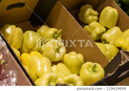 Fresh, vibrant yellow bell peppers in bulk, neatly packed within corrugated cardboard boxes, ready for retail sale at a bustling grocery market produce aisle 129424699