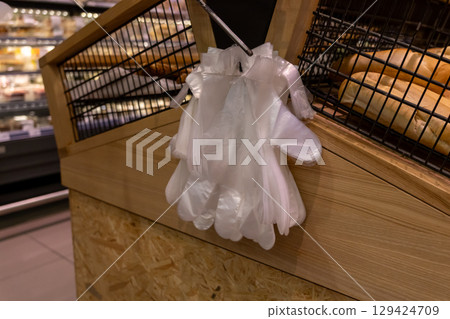 Disposable plastic gloves hanging for customer use in a supermarket bakery, ensuring food hygiene and safety for self-service shopping 129424709