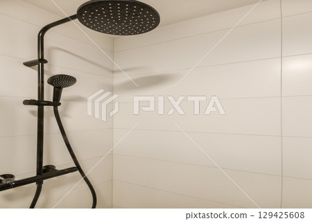 Stylish black shower fixture against clean, white tiled wall creates a sleek and modern bathroom appearance. Perfect for contemporary interiors. 129425608