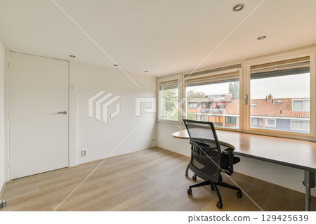 A spacious and minimalistic office interior featuring large windows that allow natural light to flood in, creating an open and inviting atmosphere. 129425639