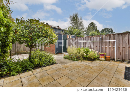 A peaceful garden featuring a variety of plants, stone pathways, and a wooden fence. The area is well-kept, providing an ideal spot for relaxation. A peaceful garden featuring a variety of plants, stone pathways, and a wooden fence. The area is well-kept, providing an ideal spot for relaxation. 129425686