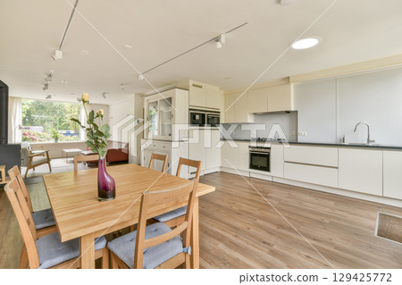 A spacious kitchen and dining area featuring modern appliances, wooden flooring, and natural light illuminating the space creates a welcoming atmosphere. 129425772