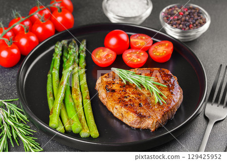 Grilled beef steak with asparagus and cherry tomatoes on black plate, gourmet healthy dinner 129425952