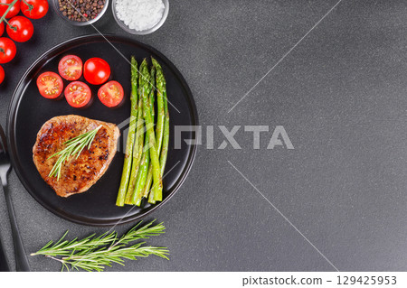 Grilled beef steak with asparagus and cherry tomatoes on black plate on gray background, copy space Grilled beef steak with asparagus and cherry tomatoes on black plate on gray background, copy space 129425953