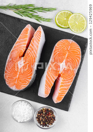 Fresh raw salmon or trout steaks with tomatoes, spices, rosemary and lime on white stone background 129425969