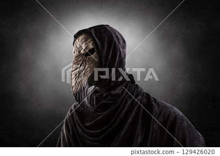 Creepy figure with long bird beak mask in hooded cloak at night over dark misty background Creepy figure with long bird beak mask in hooded cloak at night over dark misty background 129426020