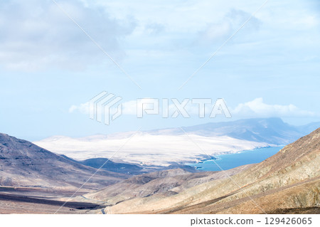 A desolate, dry, bare mountain under bright sunlight, with the sea visible in the distance. Inland on the island of Fuerteventura A desolate, dry, bare mountain under bright sunlight, with the sea visible in the distance. Inland on the island of Fuerteventura 129426065