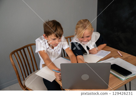 Children Laptop Classroom Learning: Two children studying together on a laptop at a desk in a classroom setting. Children Laptop Classroom Learning: Two children studying together on a laptop at a desk in a classroom setting. 129426231