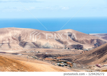 A desolate, dry, bare mountain under bright sunlight, with the sea visible in the distance. Inland on the island of Fuerteventura A desolate, dry, bare mountain under bright sunlight, with the sea visible in the distance. Inland on the island of Fuerteventura 129426272