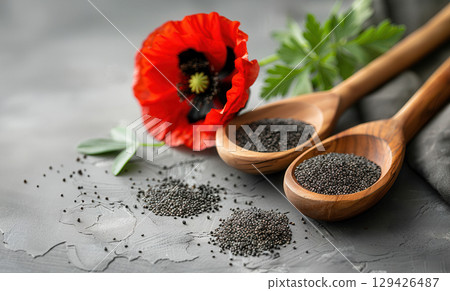 Wooden spoons with poppy seeds and red poppy flower on a grey background 129426487