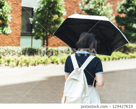 一名女學生背著書包，打著陽傘，走在上學的路上 129427619
