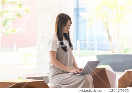 一名女學生在學校長椅上用筆記型電腦工作 一名女學生在學校長椅上用筆記型電腦工作 129427675