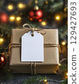 Festive wrapped gift with blank tag and holiday decorations in soft colorful lighting, New Year's present packed in brown craft paper 129427693
