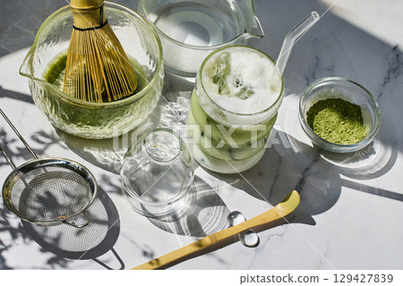 Refreshing Matcha Setup. A sunlit arrangement of matcha tea tools with a frothy iced matcha latte. Refreshing Matcha Setup. A sunlit arrangement of matcha tea tools with a frothy iced matcha latte. 129427839