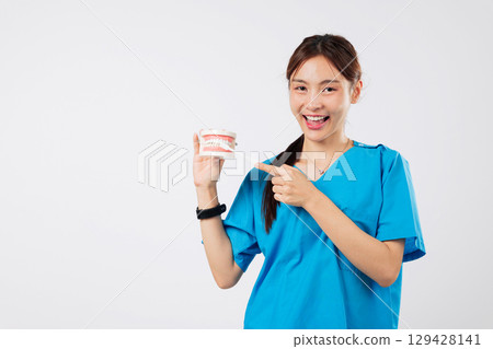 Smiling Asian dentist woman presents a model of teeth, demonstrating the proper brushing technique, using toothbrush so you can keep your teeth healthy and strong, headshot isolated white background 129428141