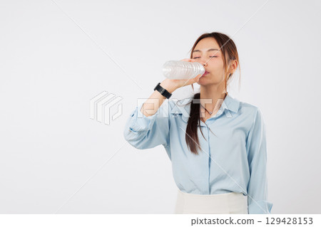 Young woman drink bottle water hold eyes closed, asian girl enjoying her refreshing drink from a plastic bottle for hydration, smiling and positive, isolated studio white background 129428153