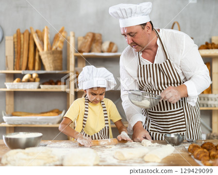 Bakers dad teaches daughter niece to work with dough, using rolling pin 129429099