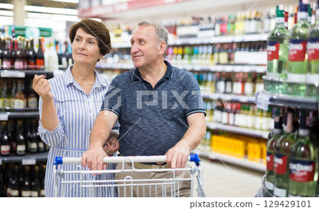 Mature couple husband and wife choose alcoholic drinks in supermarket Mature couple husband and wife choose alcoholic drinks in supermarket 129429101
