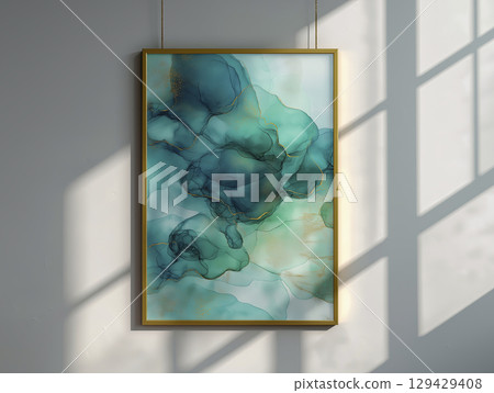Modern abstract art piece with flowing blue and green ink patterns accented by gold lines, hanging in minimalistic frame on light colored wall with sunlight casting shadows 129429408
